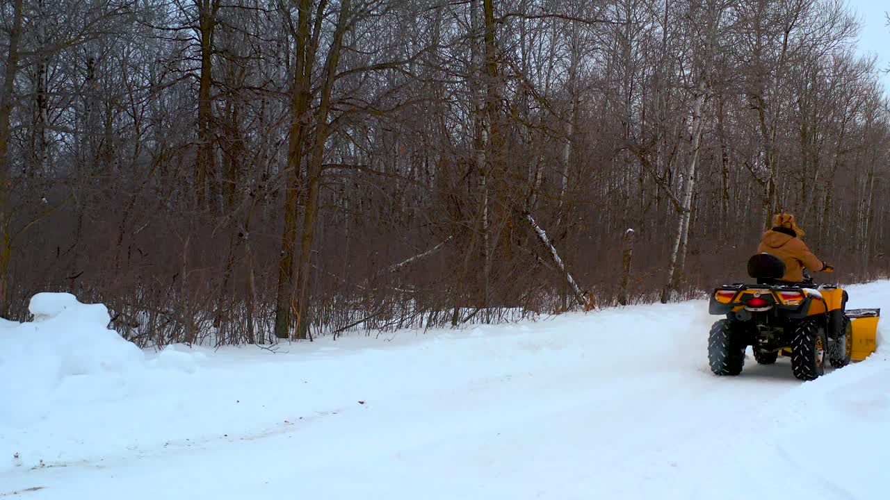 Un uomo rimuove la neve dal suo vialetto con un ATV in una proprietà rurale canadese