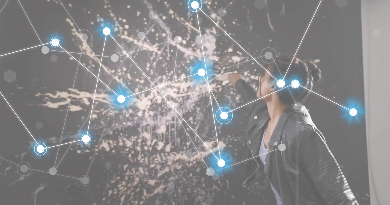 Female artist holding brush to activate node overlay, dipping into pail and flicking splatter art