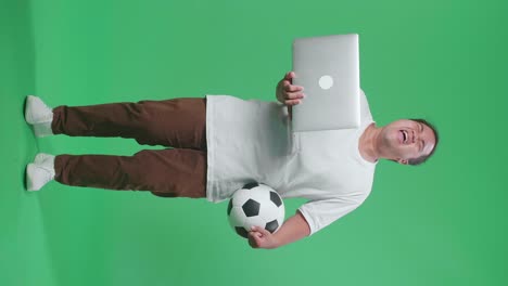 cuerpo lleno de hombre asiático con una pelota está gritando gol estar feliz por el equipo ganador mientras aplaude el fútbol en una computadora portátil en el estudio de pantalla verde