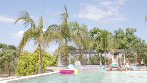 Happy-caucasian-father-with-son-sitting-and-playing-at-swimming-pool