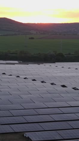 beautiful vertical drone footage capturing a wide solar panel field in rural bulgaria during sunset. golden light reflects off the panels, symbolizing renewable energy and sustainability.
