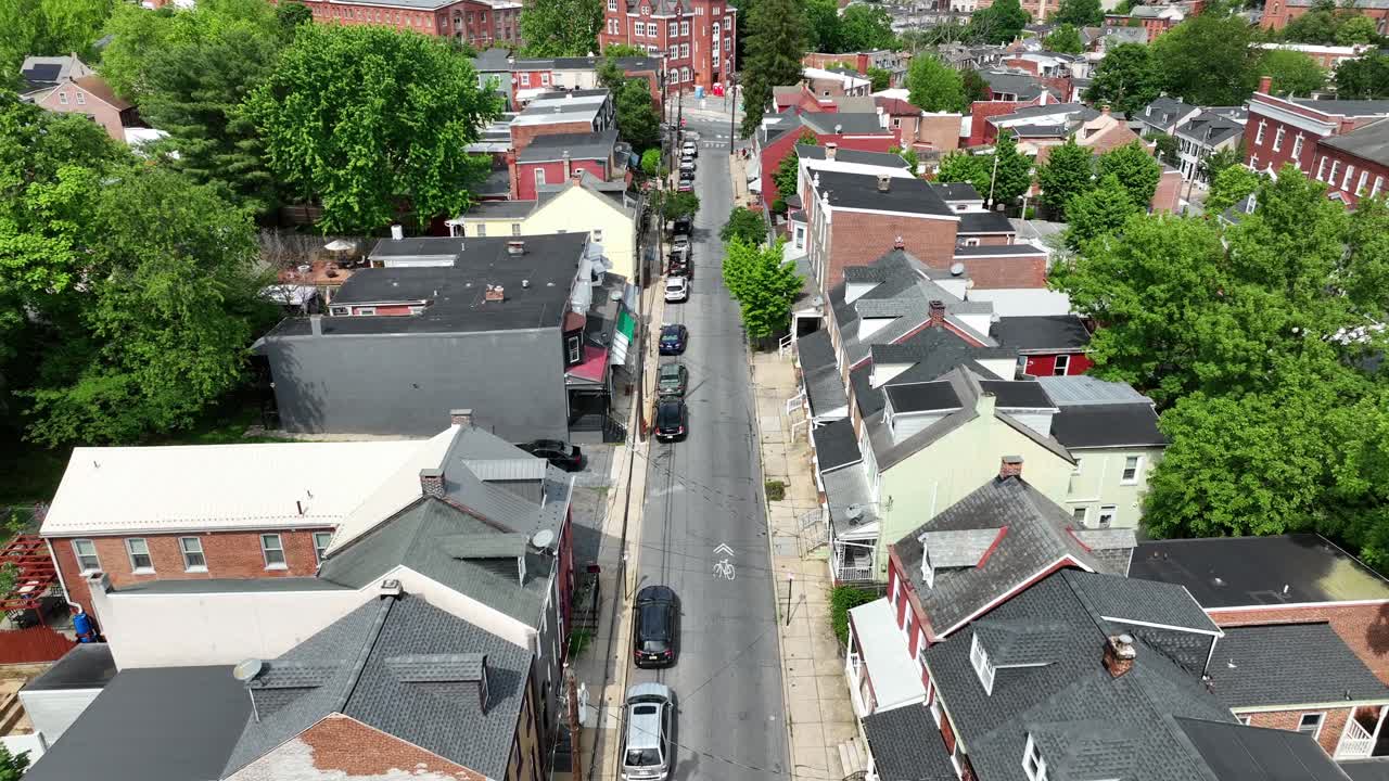 Historic homes and houses along street with parking vehicles. Sunny day with green trees in summer. Lancaster, PA, USA. Aerial birds eye shot. Rooftop of buildings with chimney.