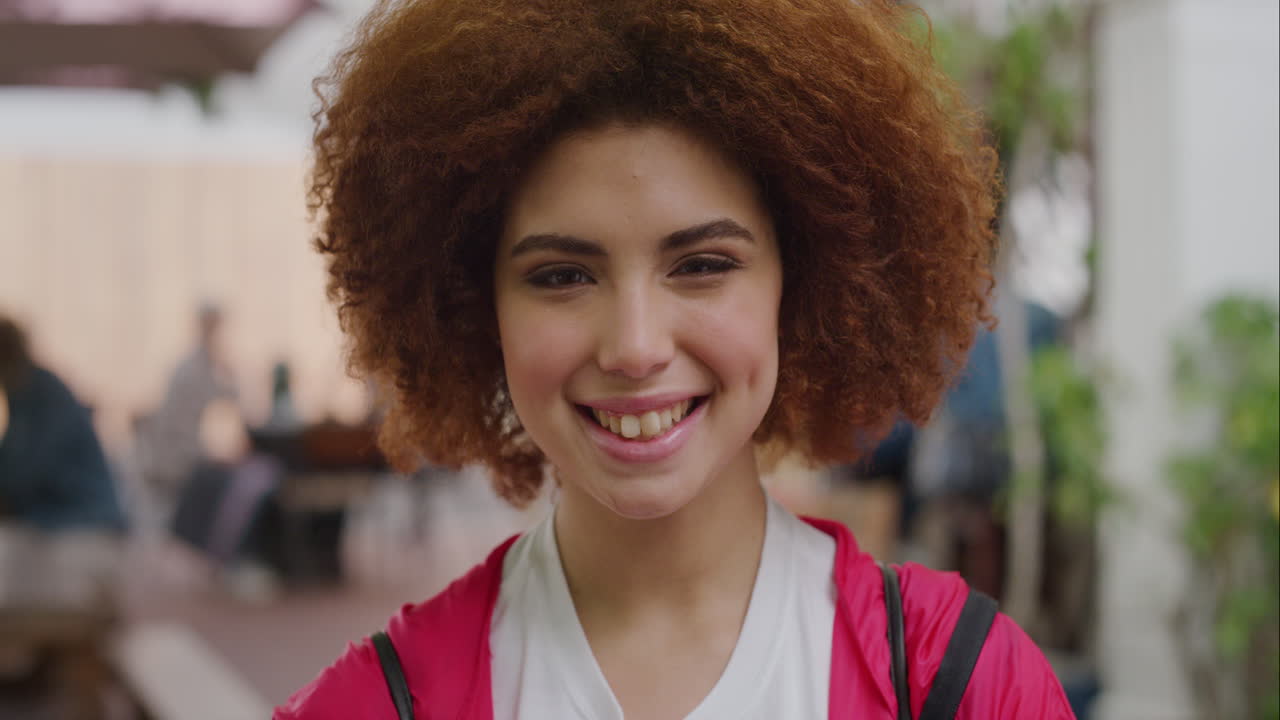 retrato de una mujer joven de raza mixta sonriendo alegremente mirando a la cámara disfrutando de un estilo de vida feliz estudiante femenina linda con afro con chaqueta rosa en el fondo urbano