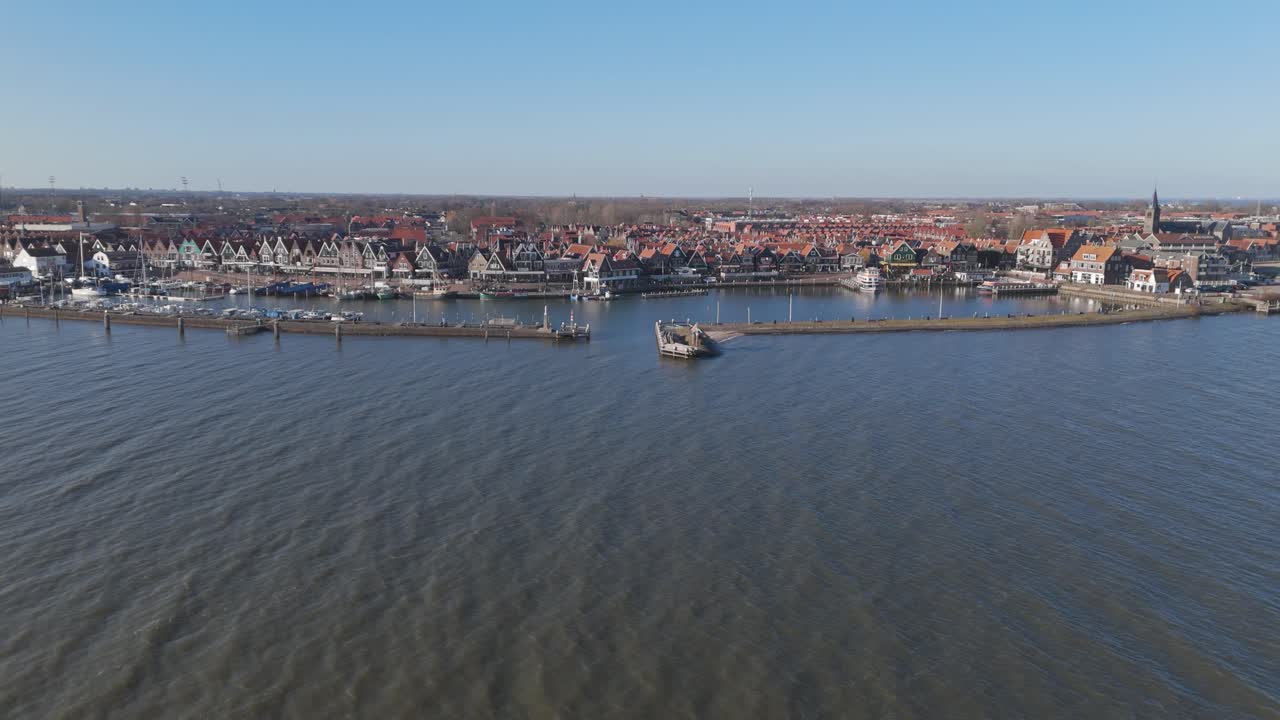 Schuine luchtdrone-opname van de Volendamse waterkant met boten, havenactiviteit en dichte Nederlandse architectuur.