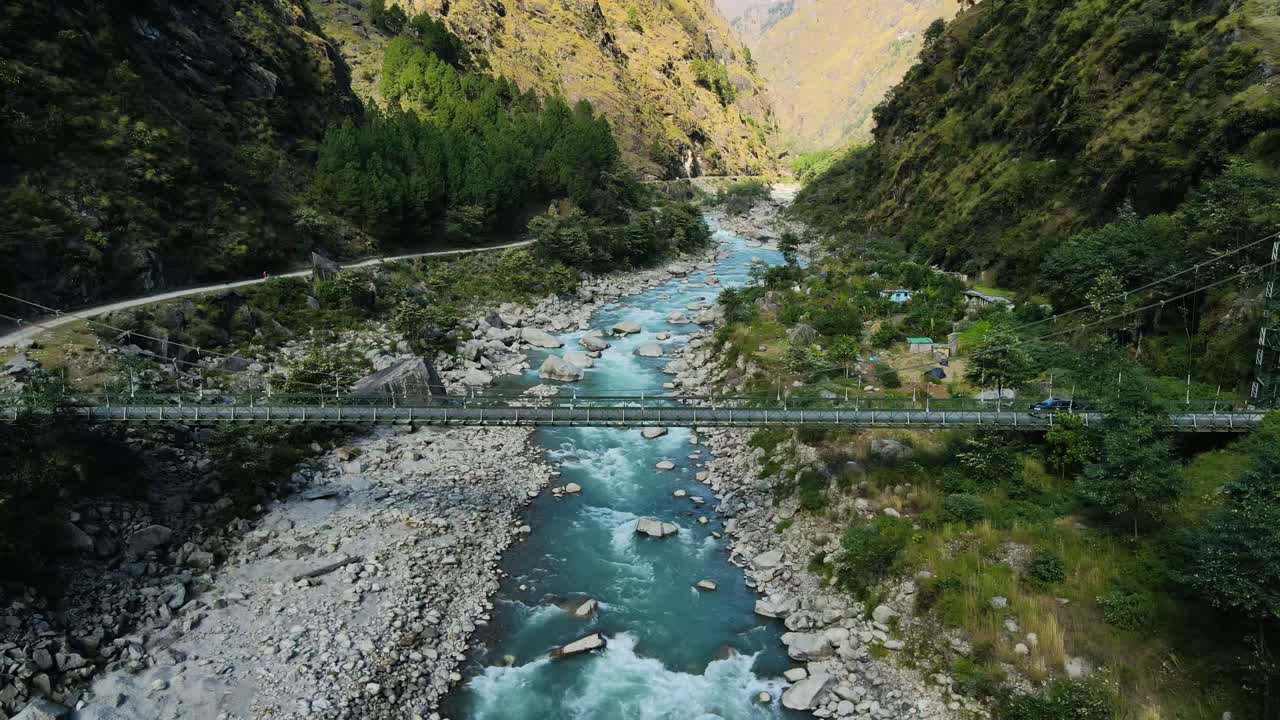 un drone aéreo captura un coche cruzando un puente sobre un río con impresionantes aguas azules debajo.
