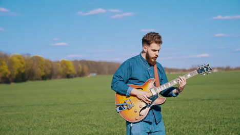 musical band outdoors. handsome guy playing the guitar and singing together with a singer on green field background in sunny day.