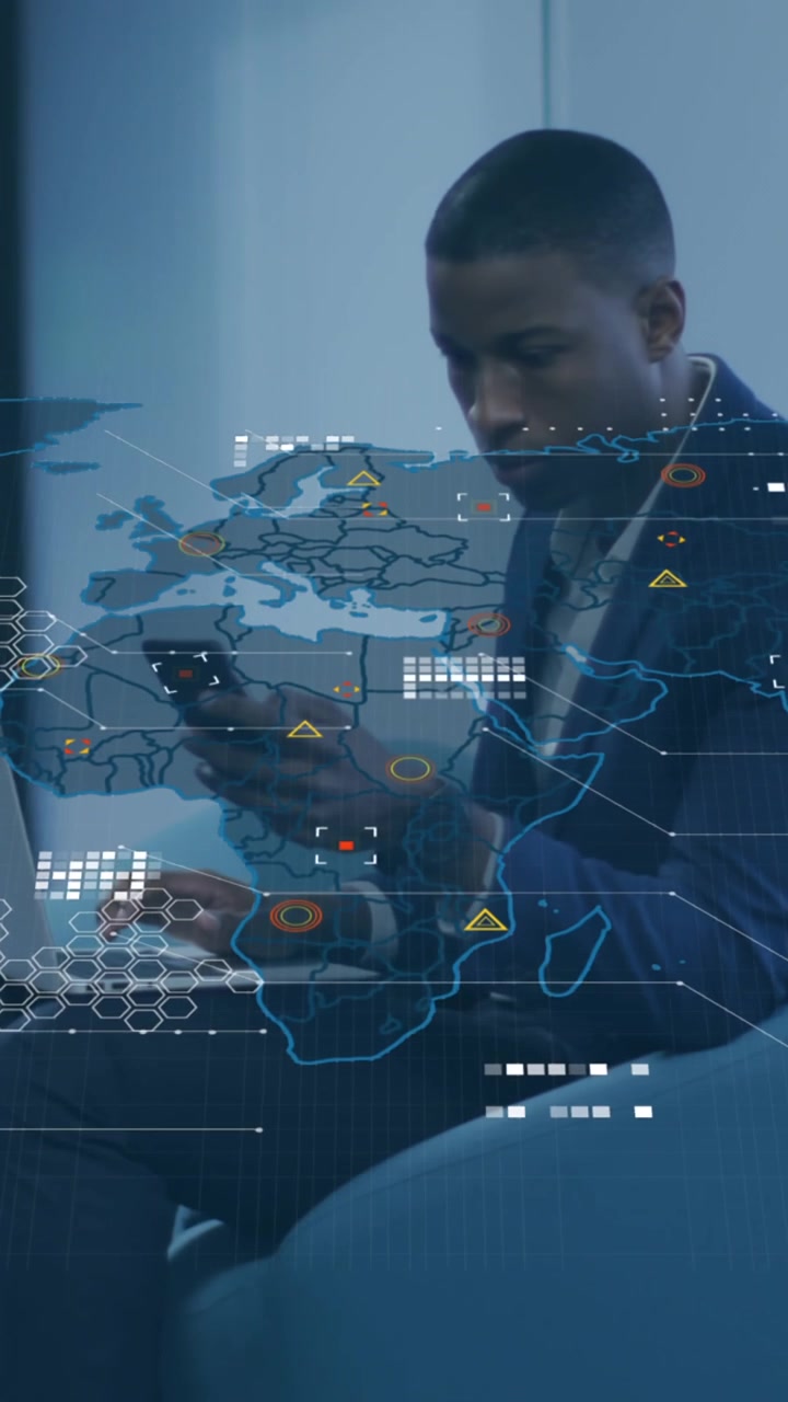Animation of world map over african american businessman with laptop using smartphone at office