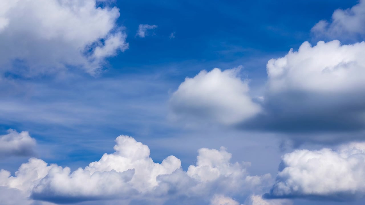 Horizonless daytime sky dominated by large white cumulus clouds across the middle of the frame with thin cirrus streaks near the top; soft sunlight casts