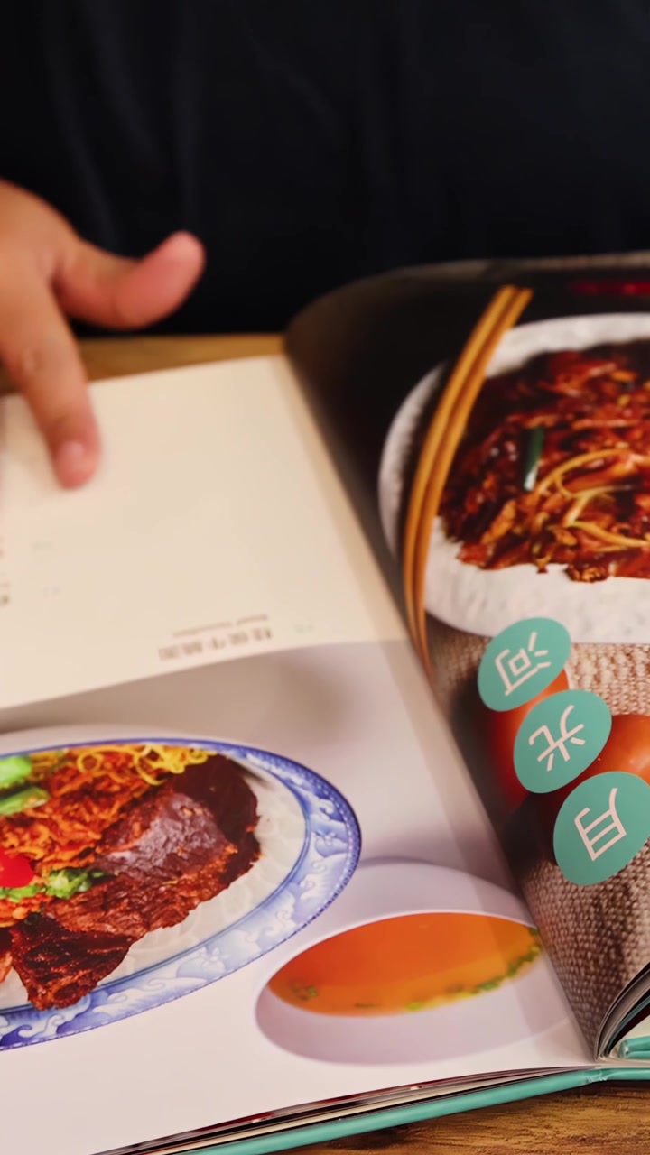 鮮やかなアジア料理と料理の盛り付けスタイルを紹介する、イラスト入りのメニューをめくる人。