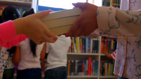 schoolgirl giving a book to a female teacher in school library 4k