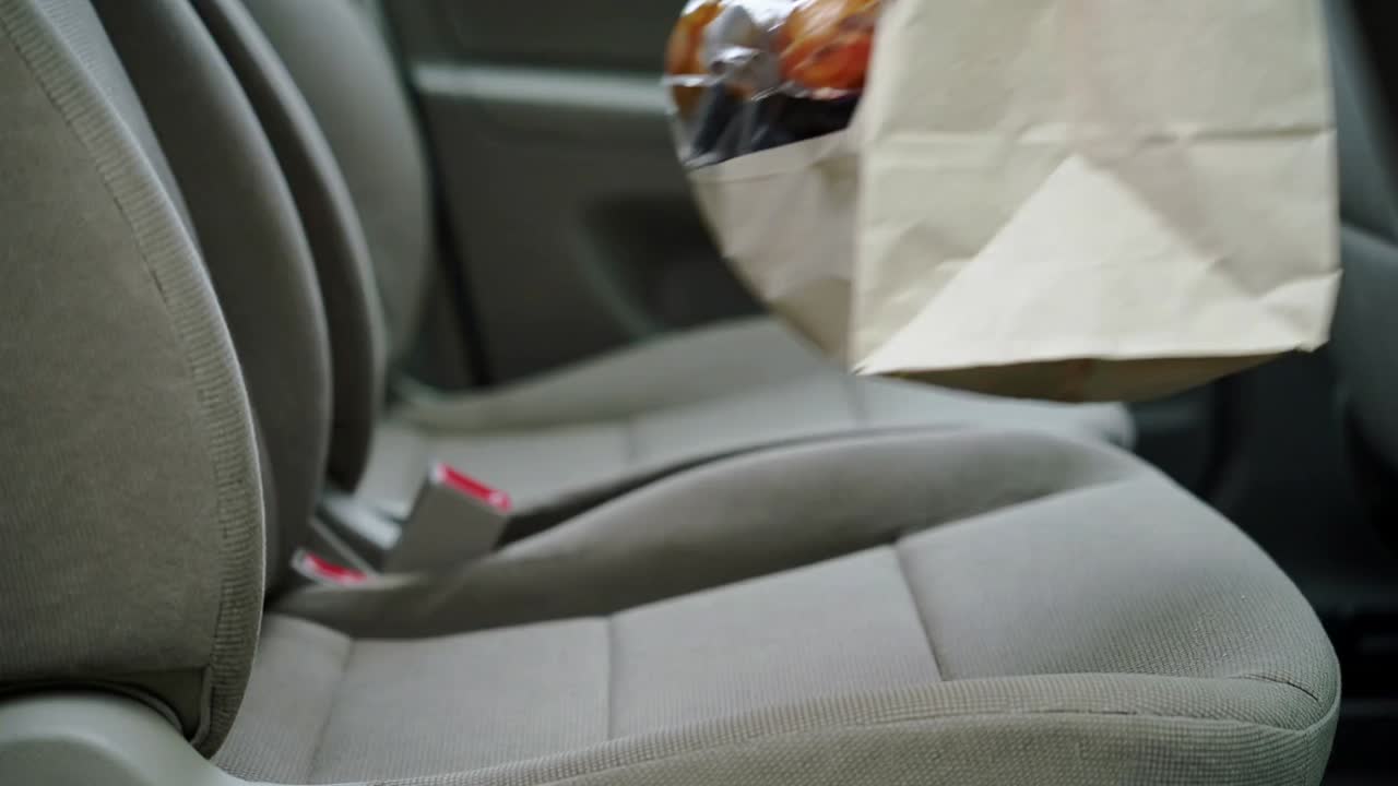 Colocación de una bolsa de papel sobre el asiento del copiloto, manos con los brazos descubiertos abriendo y organizando naranjas
