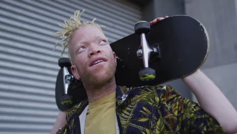 feliz albino hombre afroamericano con dreadlocks caminando y sosteniendo patineta