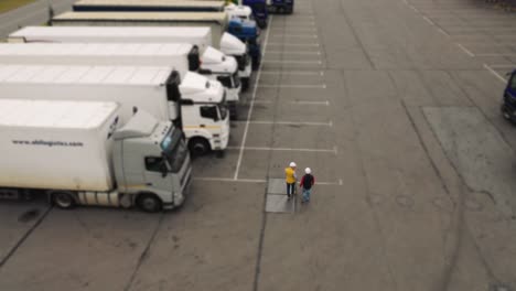 aerial. camera moving around two workers, two drivers works on tablet near trucks.