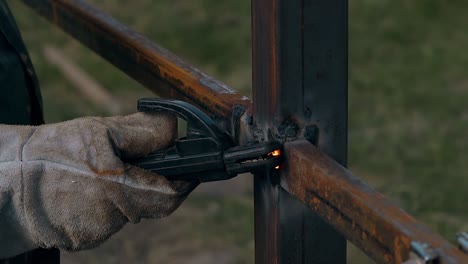 close view repairman in gloves welds metal rail to pole