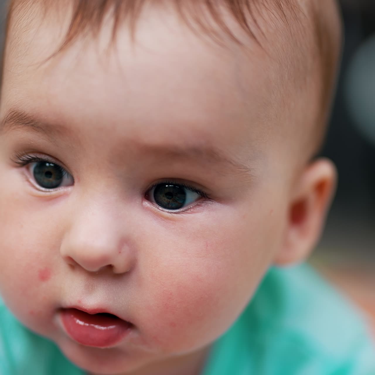 Happy cheerful resilient baby boy lies on belly in front of camera. Face portrait of a lovely child with plump cheeks