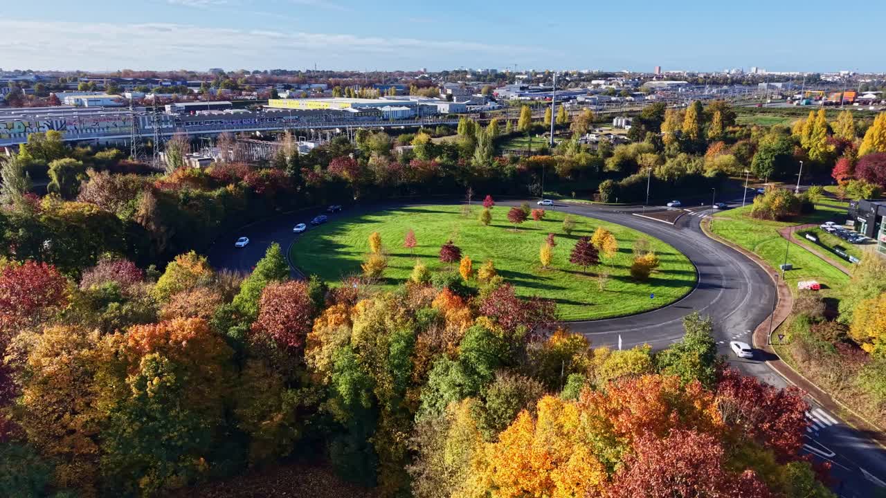 Drone shot flying forward toward a large roundabout surrounded by colorful autumn trees and moving vehicles in Cesson-Sévigné, France, on a sunny day