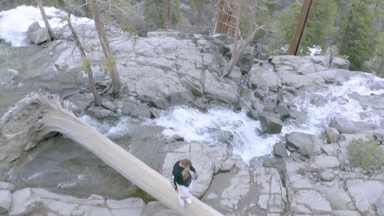 hombre caminando sobre un tronco de madera muerto junto a la cascada