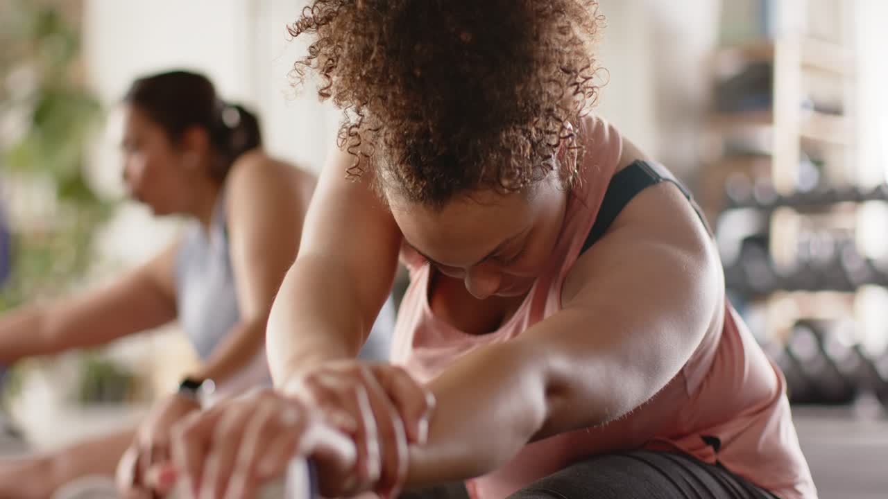 At instructor cue, woman grasping shoe and deepening stretch on yoga mat in studio for flexibility