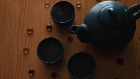 minimal background of a green japanese tea set with steam coming out of the cups, on a wooden table, with some stones around