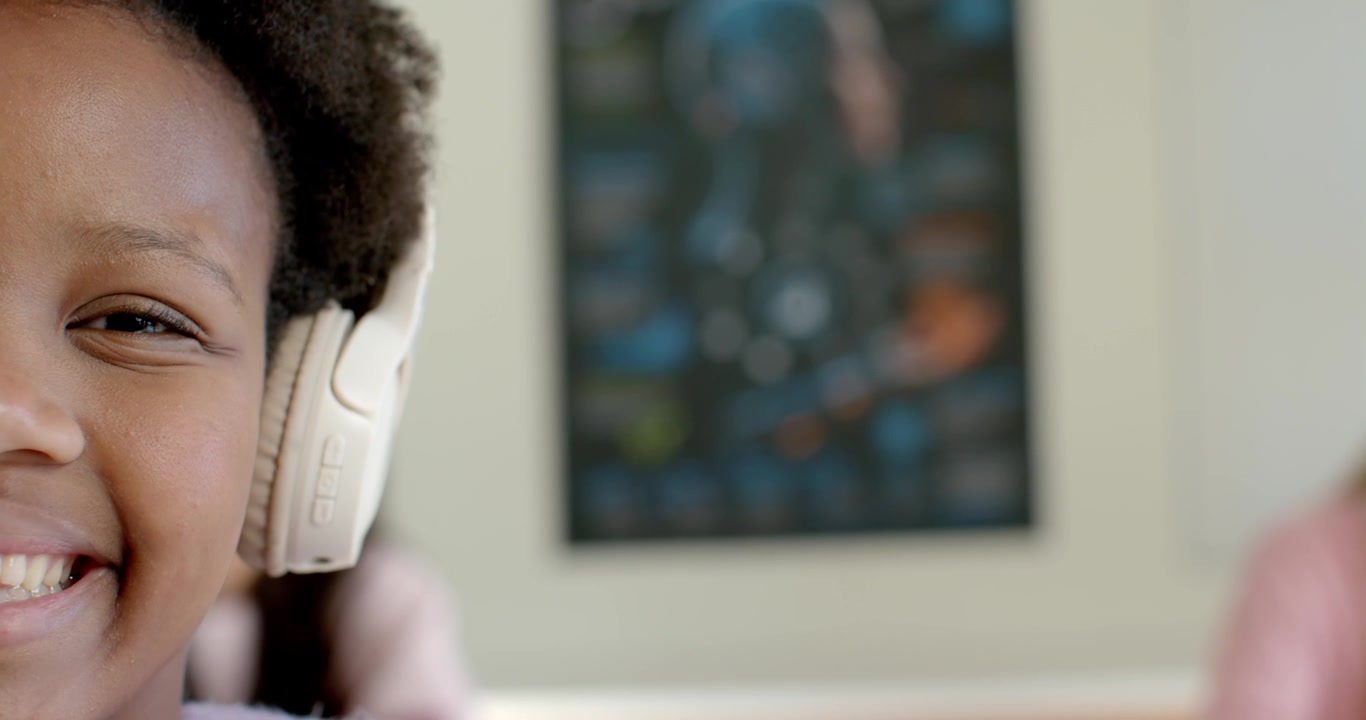 African American teen female listening as song starts on white headset, smiling at home, copy space