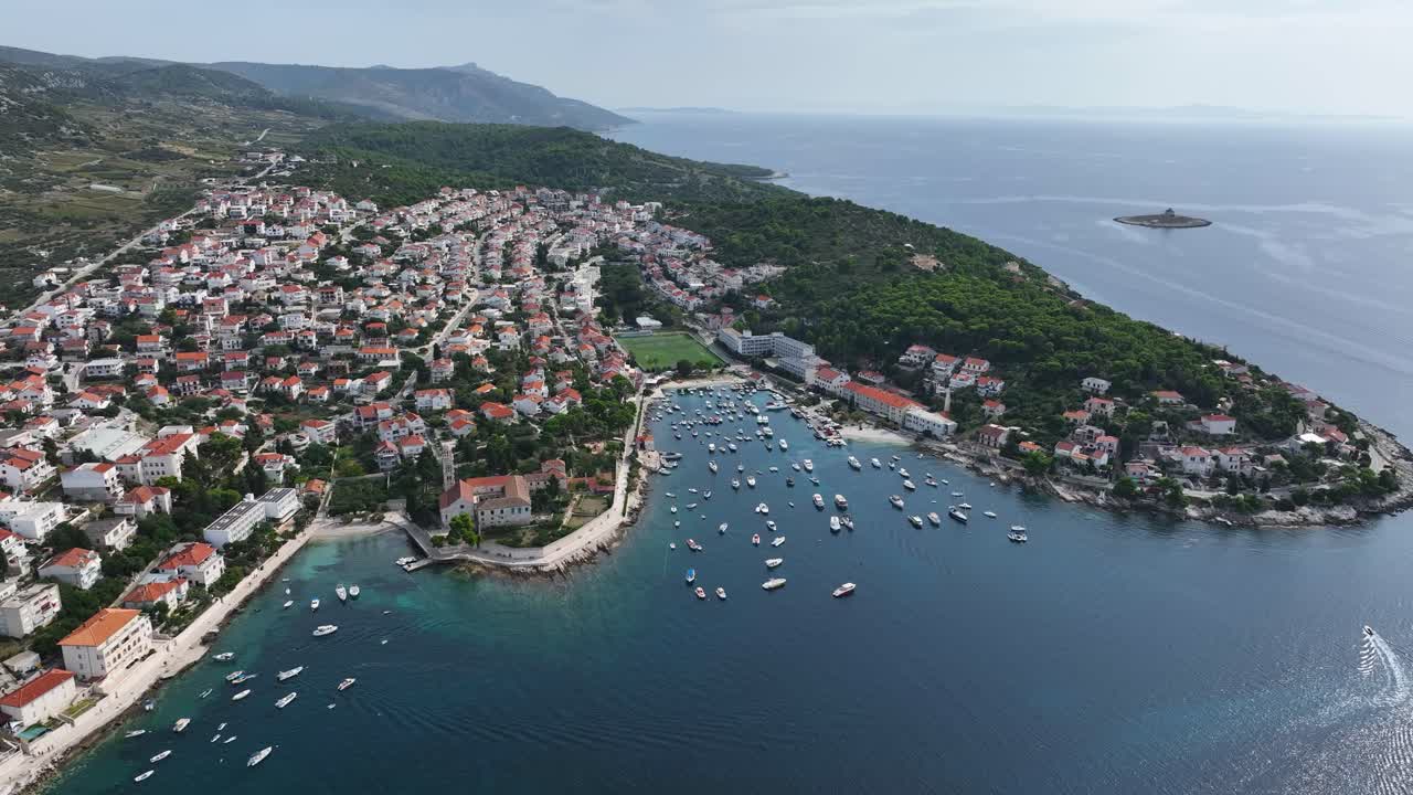 Picturesque Town And Harbor Of Hvar Surrounded By Adriatic Sea During Daytime In Croatia. Aerial, Pull-Back Shot