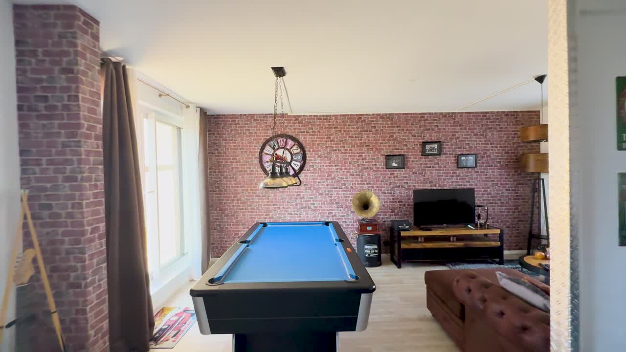Camera glides through a sunlit, vintage-inspired lounge featuring a blue pool table, exposed brick walls, antique decor, and modern furnishings in a cozy apartment