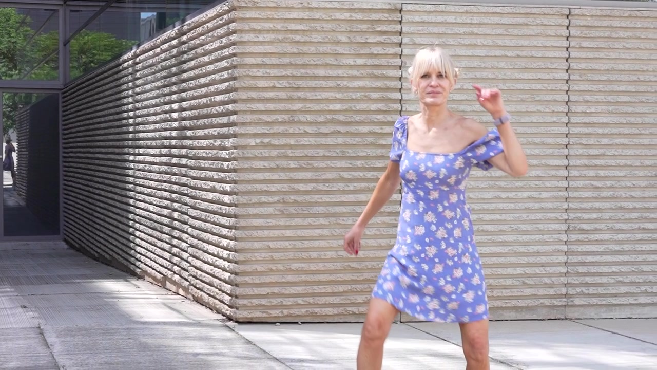 Una donna balla con grazia all'aperto in una giornata luminosa, vestita con un bellissimo abito floreale blu.
