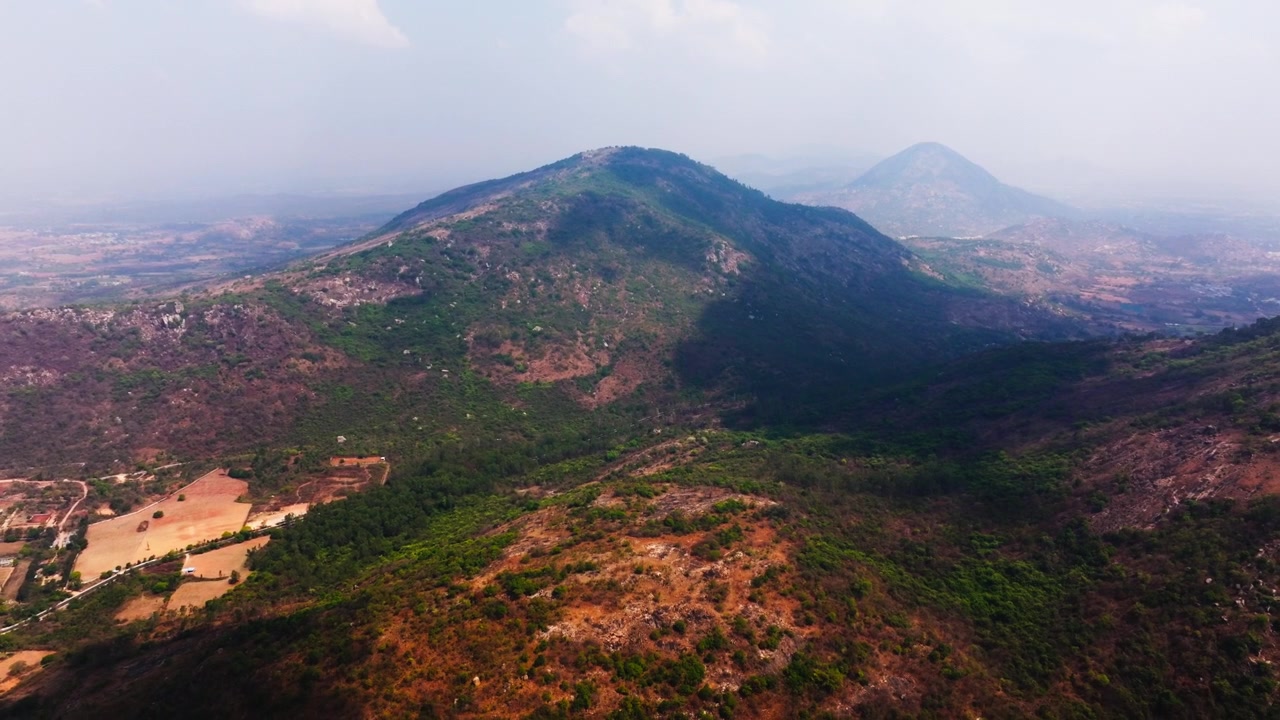Bjerge med tåge, dis, himmel, grønne områder og landsby ved Nandi Hills, Bengaluru, Karnataka, Indien. Dagtimer, tilbagetrækkende droneoptagelse, 4K.