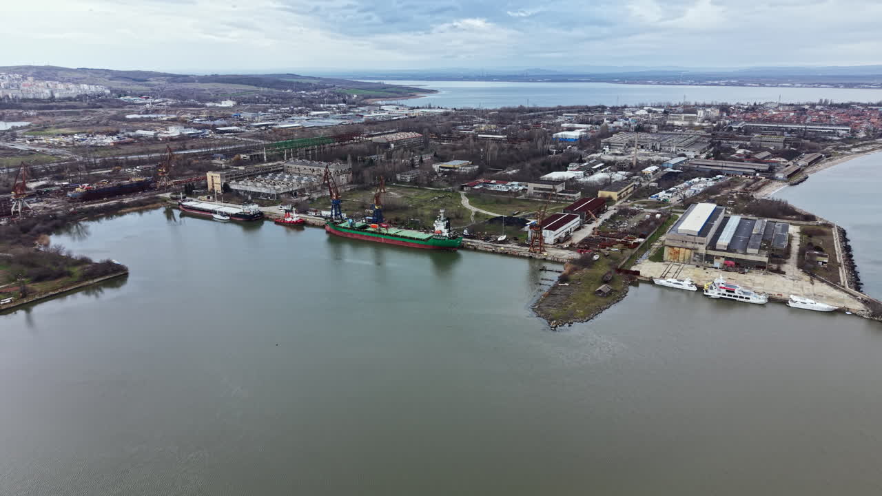 Vista di un fiume con navi attraccate lungo la riva in un'area portuale, di giorno, in una città costiera con edifici e siti industriali nelle vicinanze