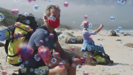 animación de células de covid-19 flotando sobre una pareja mayor con máscara facial y mochila en la playa