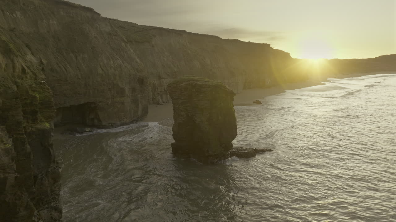 Rock pinnacle at New Zealand Fortrose cliffs during bright sunrise, aerial