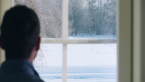 Man-in-shirt-sips-coffee,-looks-out-window-at-winter-scene