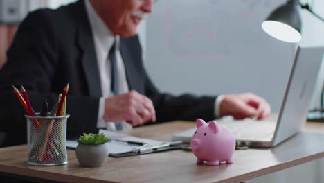 piggy bank, senior business man accountant typing on laptop computer calculating money income