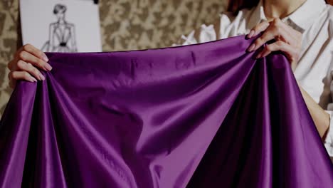 Close-up angle of a designer holding purple fabric, with a fashion sketch in the background