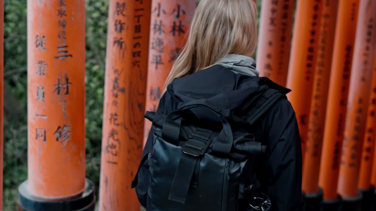A woman strolls through the iconic torii gates of Fushimi Inari Shrine in Kyoto, Japan.
