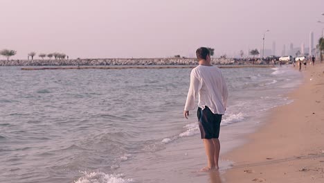 man-in-loose-shirt-stands-in-water-on-beach-slow-motion