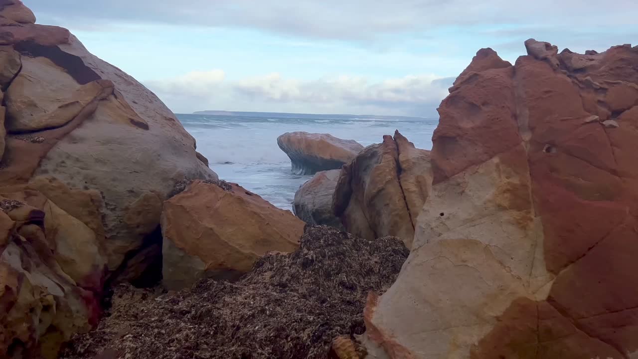 caminar a través del video sobre la formación rocosa en la playa, las olas del mar se estrellan contra la orilla de la costa