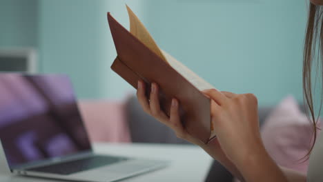 Female-student-holds-book-flipping-pages-to-find-information