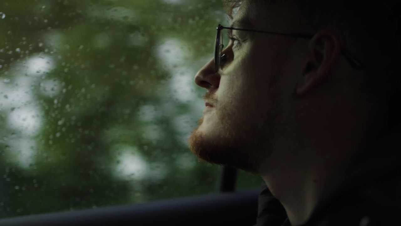 Pensive young man looks through moving car window on a rainy day