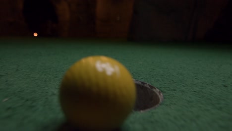 a yellow mini golf ball falls into the golf hole and bounces in the pocket on a course