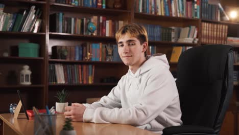 The-guy-is-sitting-in-a-chair-at-the-table,-he-is-in-a-good-mood,-and-he-is-smiling