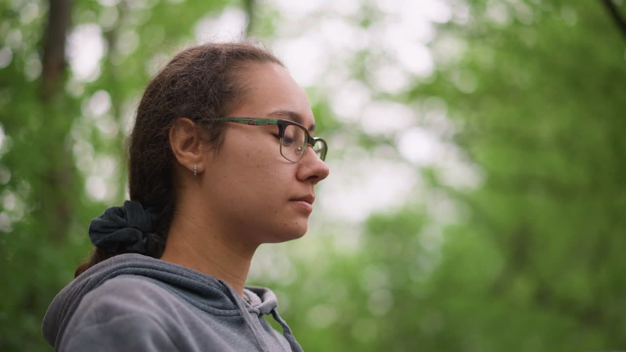 Cyclist Adjusts Helmet Strap In Forest, Focused Preparation For Ride With Gloves And Glasses, Hoodie Pulled Back, Serene Green Background, Closeup Profile Showing Careful Fit Check And Calm