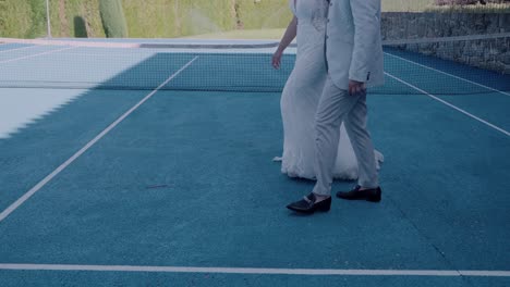 bride's gown flows elegantly as the couple walks across a blue tennis court