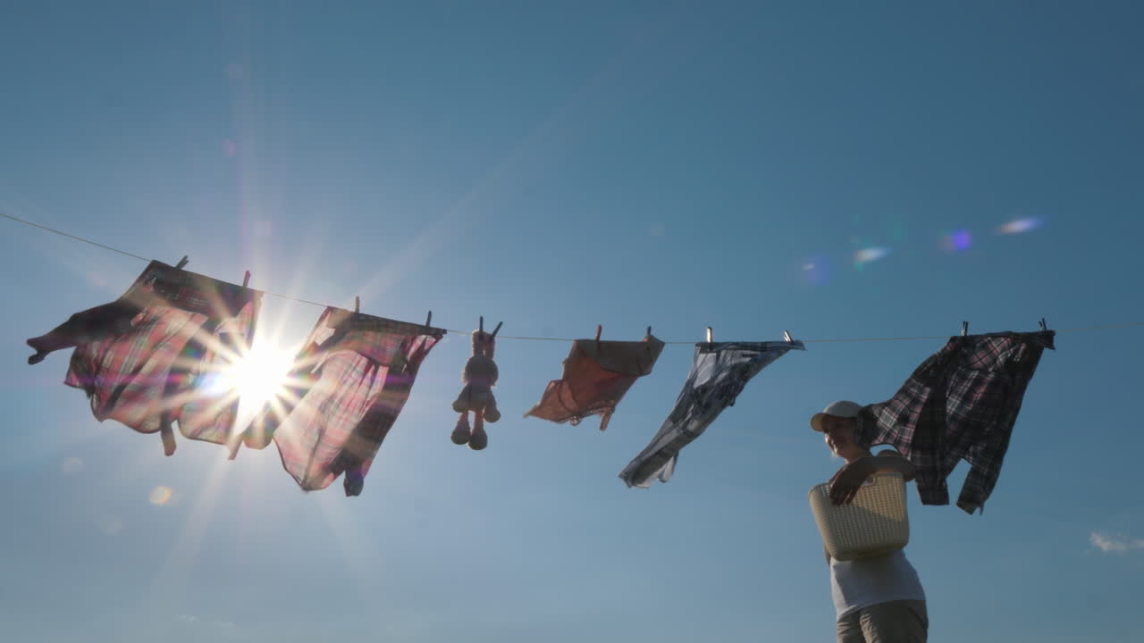 바구니를 든 여자는 밧줄에 젖은 옷을 걸고 있는 것처럼 보입니다 4k 비디오