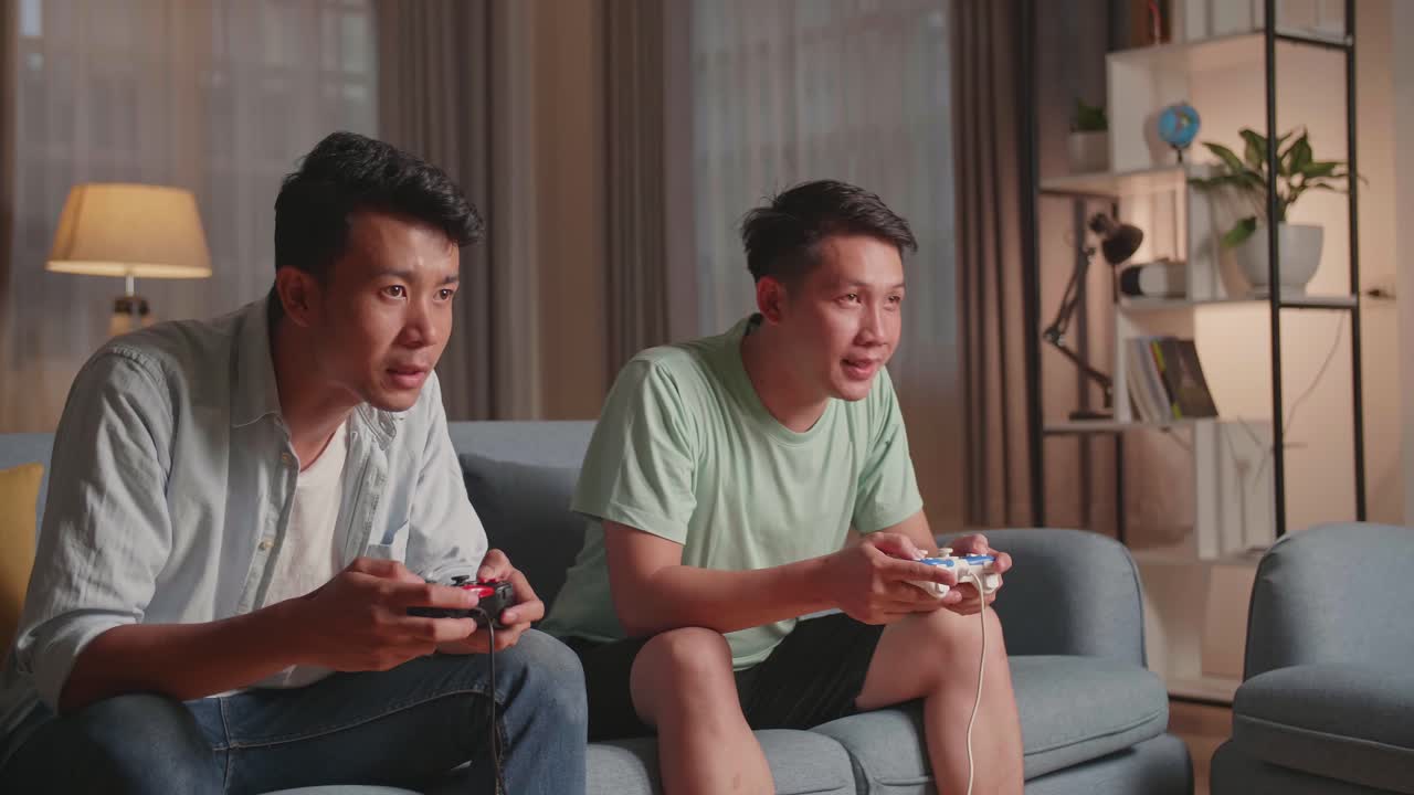 Asian Friends Playing Video Games At Home. Male Happy To Win Victory And Another Man Feeling Disappointed