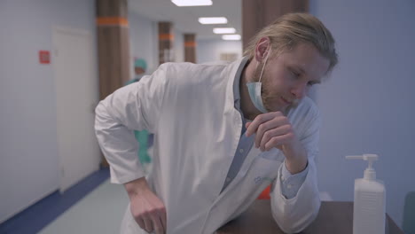 un joven médico exhausto con cabello largo y rubio está muy estresado después de un día difícil de malas noticias