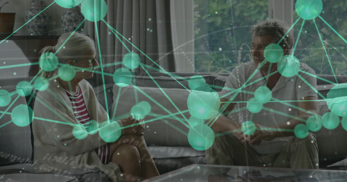 Senior couple sitting on sofa starting pulsing green network overlay and discussing tech visuals