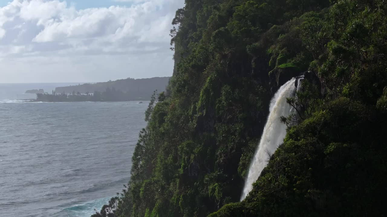 Waterfall flowing from cliff with lush greenery of Maui north shore from road to Hana, Hawaii