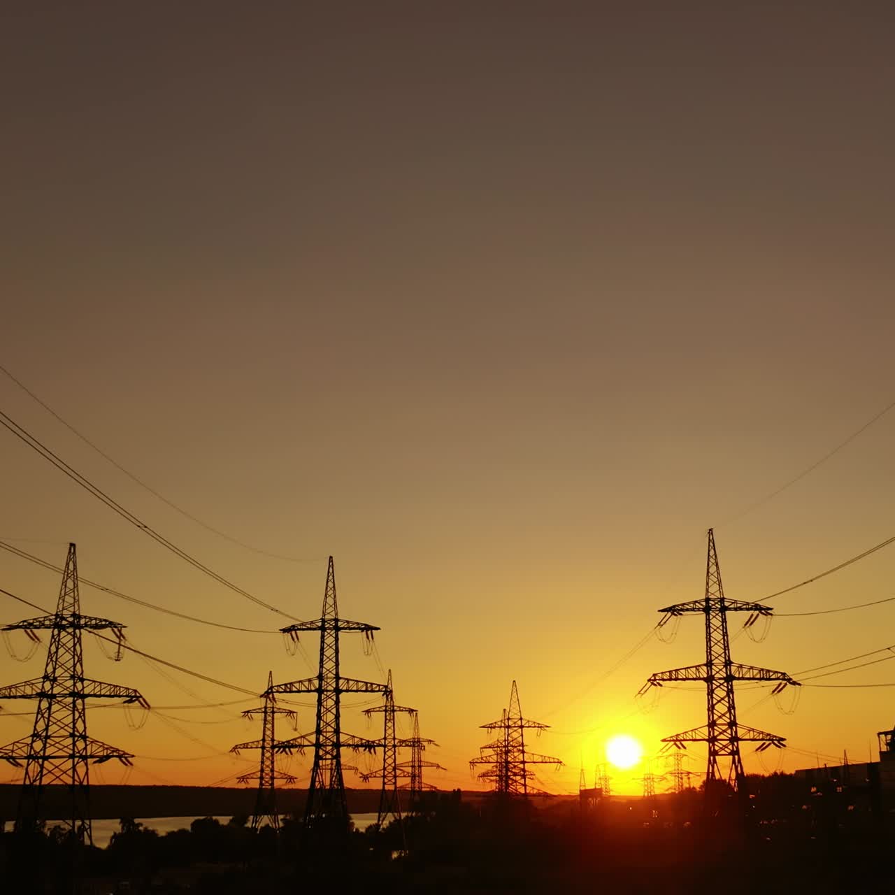 Sunset among high voltage towers. Transmission lines on the setting sun background. Electricity distribution in the evening. Motion camera back.