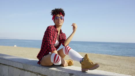 mujer joven de moda relajándose en una pared frente al mar